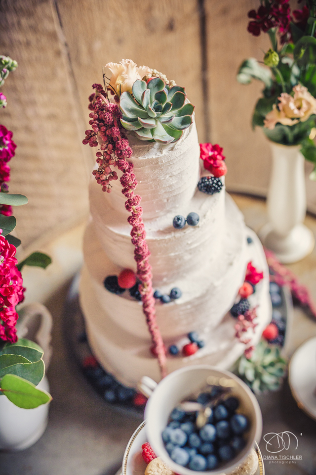 Hochzeitstorte mit Beeren und Blumen fuer eine Hochzeit in einer Scheune