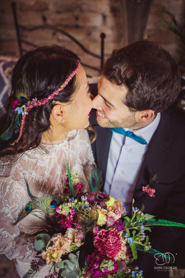 Braeutigam und Braut mit tollem buntem Brautstrauss kuessen sich bei einer Hochzeit in einer Scheune