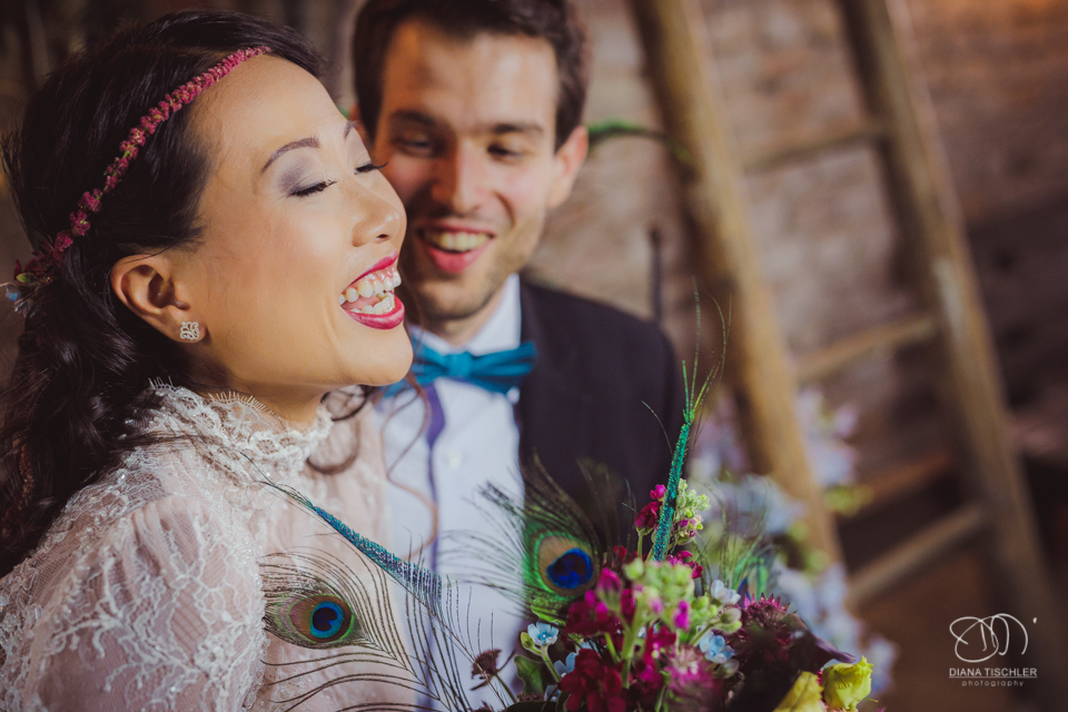 Braeutigam und Braut mit tollem buntem Brautstrauss und mit tollem vintage Boho Kleid im Kerzenlicht bei einer Hochzeit in einer Scheune