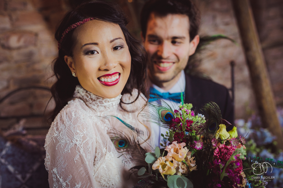 Braeutigam und Braut mit tollem buntem Brautstrauss und mit tollem vintage Boho Kleid im Kerzenlicht bei einer Hochzeit in einer Scheune