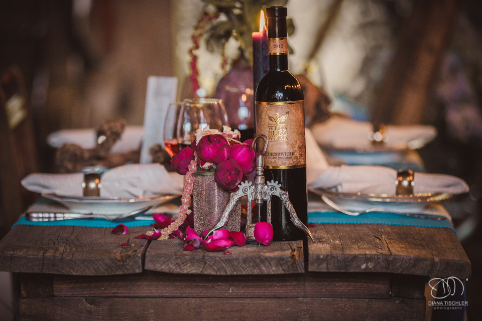 alte Weinflasche mit Flaschenoeffner und Blumen auf einem alten vintage Holz-Esstisch fuer eine Hochzeit in einer Scheune
