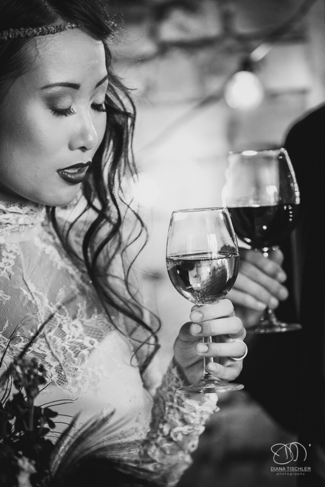 Brautpaar Schwarzweiss stoesst mit Wein an bei einer Hochzeit in einer Scheune