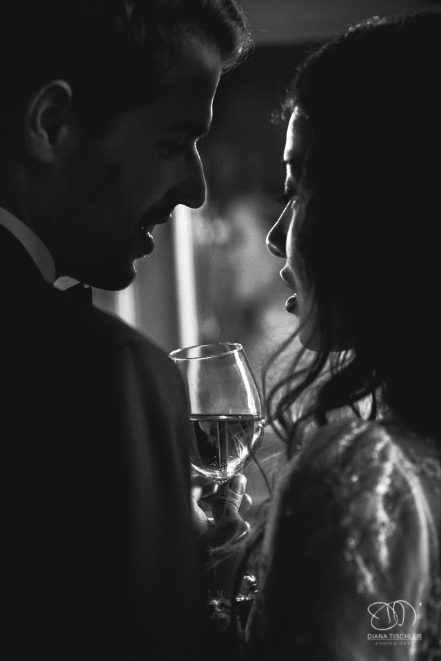 Brautpaar Schwarzweiss stoesst mit Wein an bei einer Hochzeit in einer Scheune