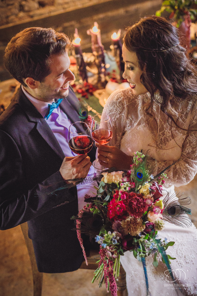 Brautpaar mit tollem buntem Brautstrauss stoesst mit Wein an bei einer Hochzeit in einer Scheune