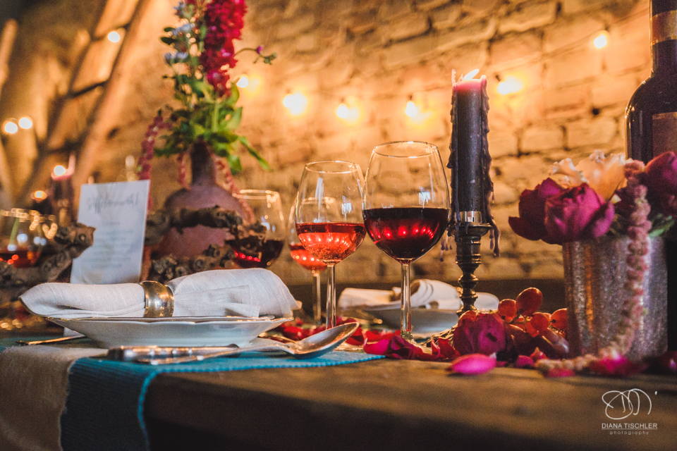 Weinglaeser und Gedeck und Blumen und Kerzen auf einem alten vintage Holz-Esstisch fuer eine Hochzeit in einer Scheune