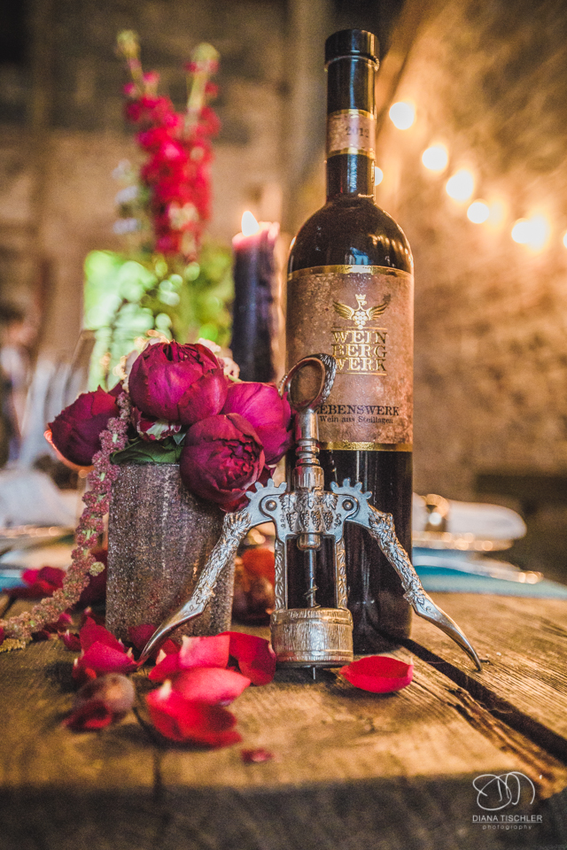 alte Weinflasche mit Flaschenoeffner und Blumen auf einem alten vintage Holz-Esstisch fuer eine Hochzeit in einer Scheune