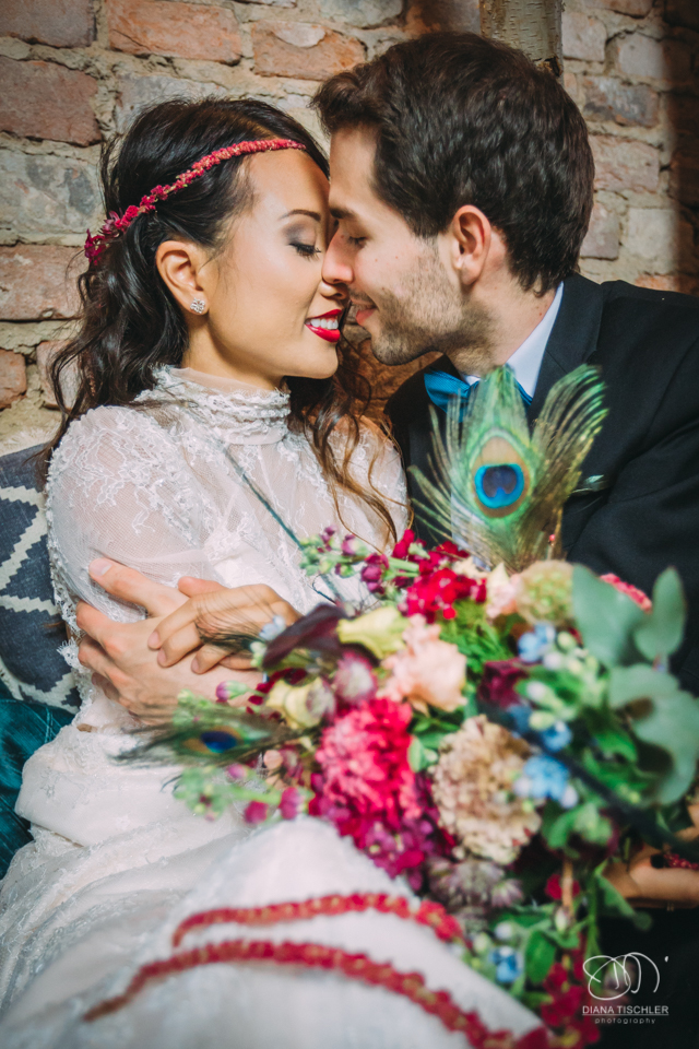 Brautpaar mit tollem buntem Brautstrauss kuesst sich bei einer Hochzeit in einer Scheune