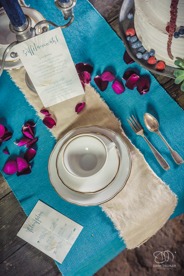 Tischgedeck mit Rosenblaettern fuer eine Hochzeit in einer Scheune