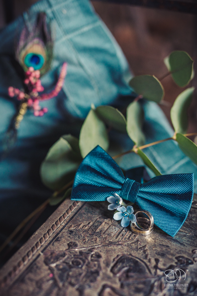 Fliege mit Ehering und Verlobungsring und Blumendeko fuer eine Hochzeit in einer Scheune
