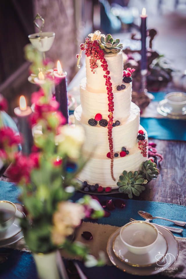 Kerzen und Hochzeitstorte mit Beeren fuer eine Hochzeit in einer Scheune