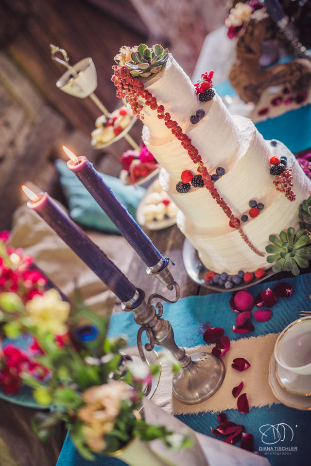 Kerzen und Hochzeitstorte mit Beeren fuer eine Hochzeit in einer Scheune