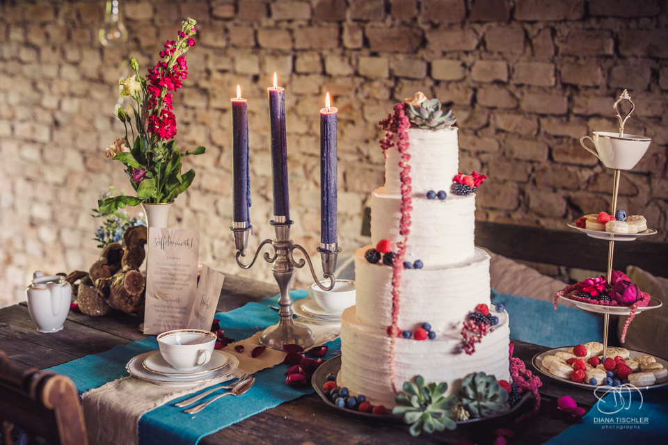 Tischgedeck Kerzen Dekoration und Hochzeitstorte fuer eine Hochzeit in einer Scheune