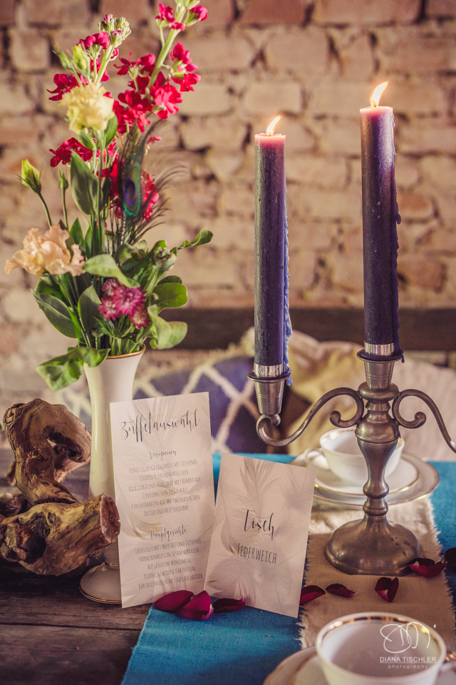 Kerzen und Papeterie mit Blumen auf einem Vintage Esstisch fuer eine Hochzeit in einer Scheune