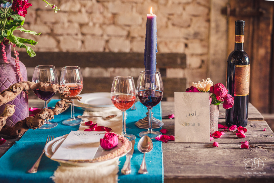 Tischgedeck und Dekoration mit Weinglaesern und Kerzen auf einem Vintage Esstisch fuer eine Hochzeit in einer Scheune