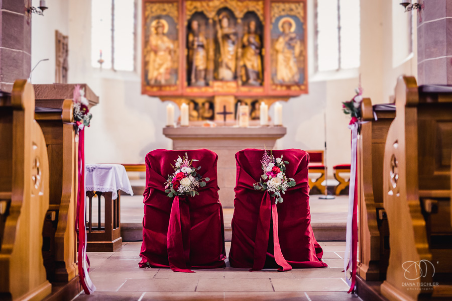 Hochzeits-Traustühle mit rotem Ueberwurf und Blumenschmuck vor dem Altar vor einer Hochzeit in der Kirche St. Ulrich in Stockheim