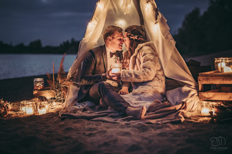 Paar im Tipi nachts am Strand mit Lichterkette und Kerzen
