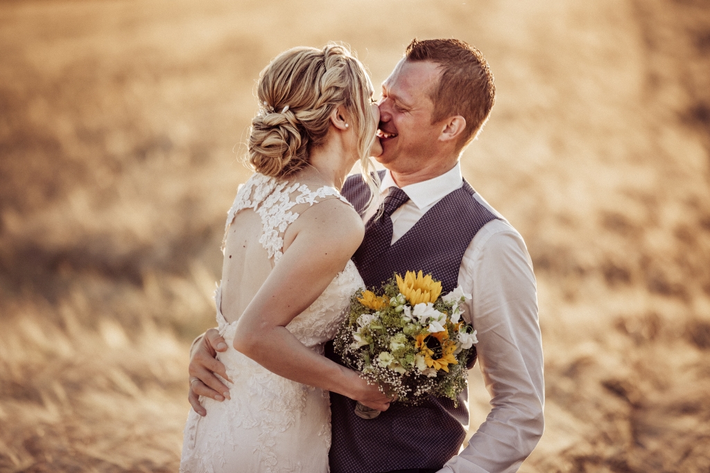 Brautpaar Kuss im Feld in tollem Licht bei Sonnenuntergang lachend Hochzeitsfotos